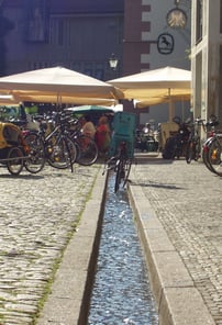 Freiburger Bächle in einer Kopfsteinpflasterstraße der Altstadt mit Fahrrädern und Straßencafés.