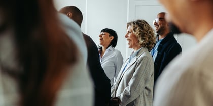 Teilnehmende einer Weiterbildung mit Namensschildern stehen lachend im Seminarraum und applaudieren