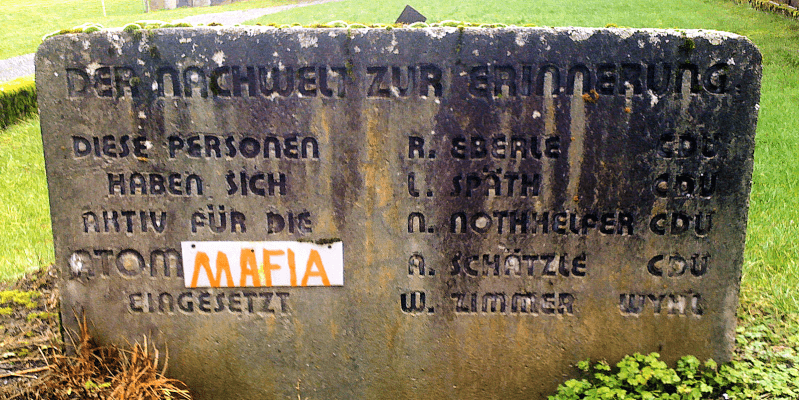Gedenkstein zum Widerstand gegen das Kernkraftwerk Wyhl bei Freiburg mit eingravierter Inschrift und einer überklebten Stelle mit dem Wort „MAFIA“.