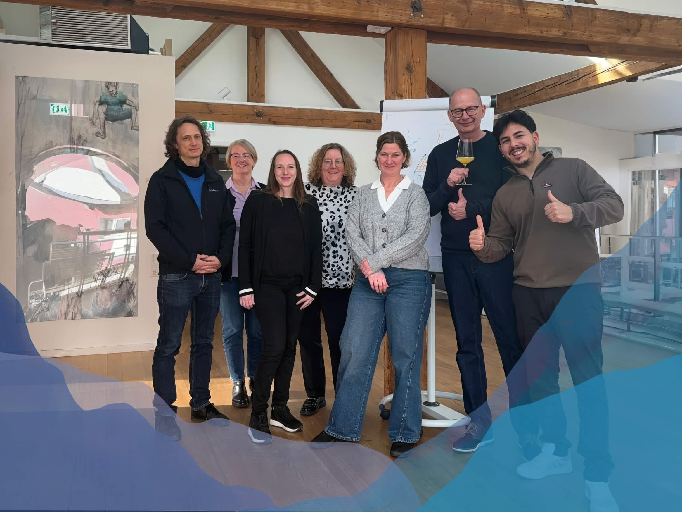 Gruppenfoto einer Mediationsausbildung in Freiburg, sieben Teilnehmende stehen lächelnd vor einem Flipchart in einem Seminarraum mit Holzbalken