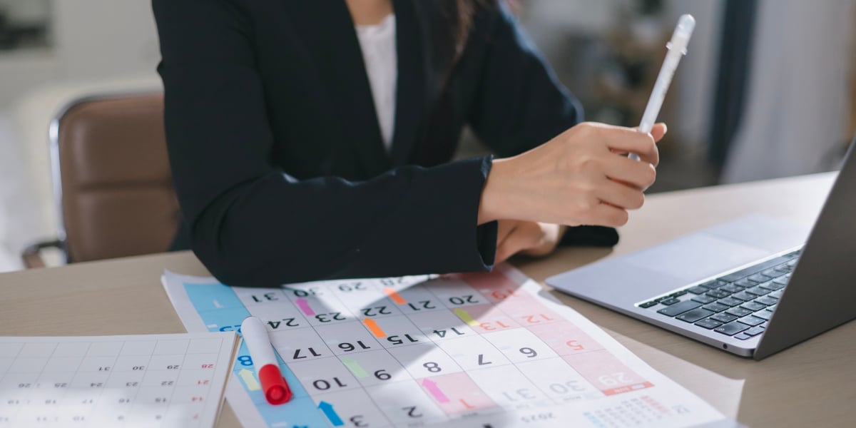 Person plant einen Zeitplan mit Kalender, Notizbuch und Laptop am Schreibtisch