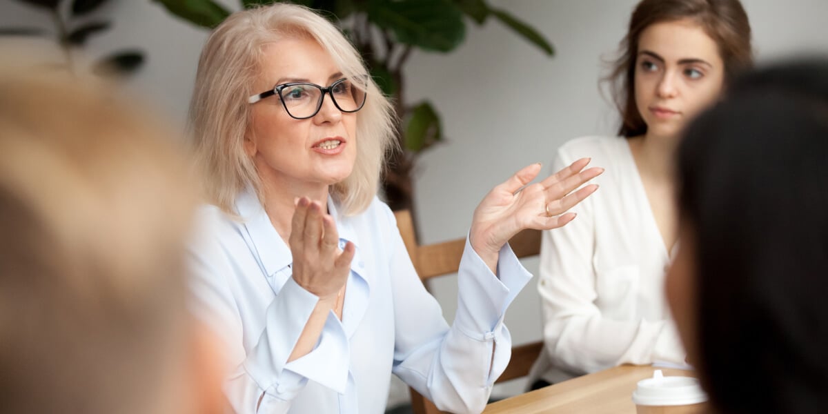 Mediatorin spricht während eines Mediationsgesprächs mit mehreren Teilnehmenden an einem Tisch.