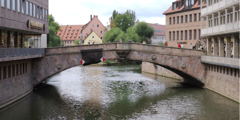 Historische Fleischbrücke über die Pegnitz in der Nürnberger Altstadt, umgeben von traditionellen und modernen Gebäuden.