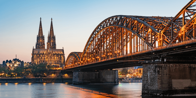 Cologne Cathedral and the Hohenzollern Bridge illuminated at sunset over the Rhine River in Cologne, Germany.