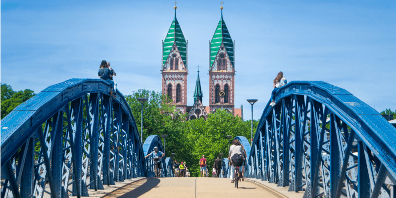 Blick über die blaue Schwabentorbrücke auf das Freiburger Münster im Stadtzentrum von Freiburg.