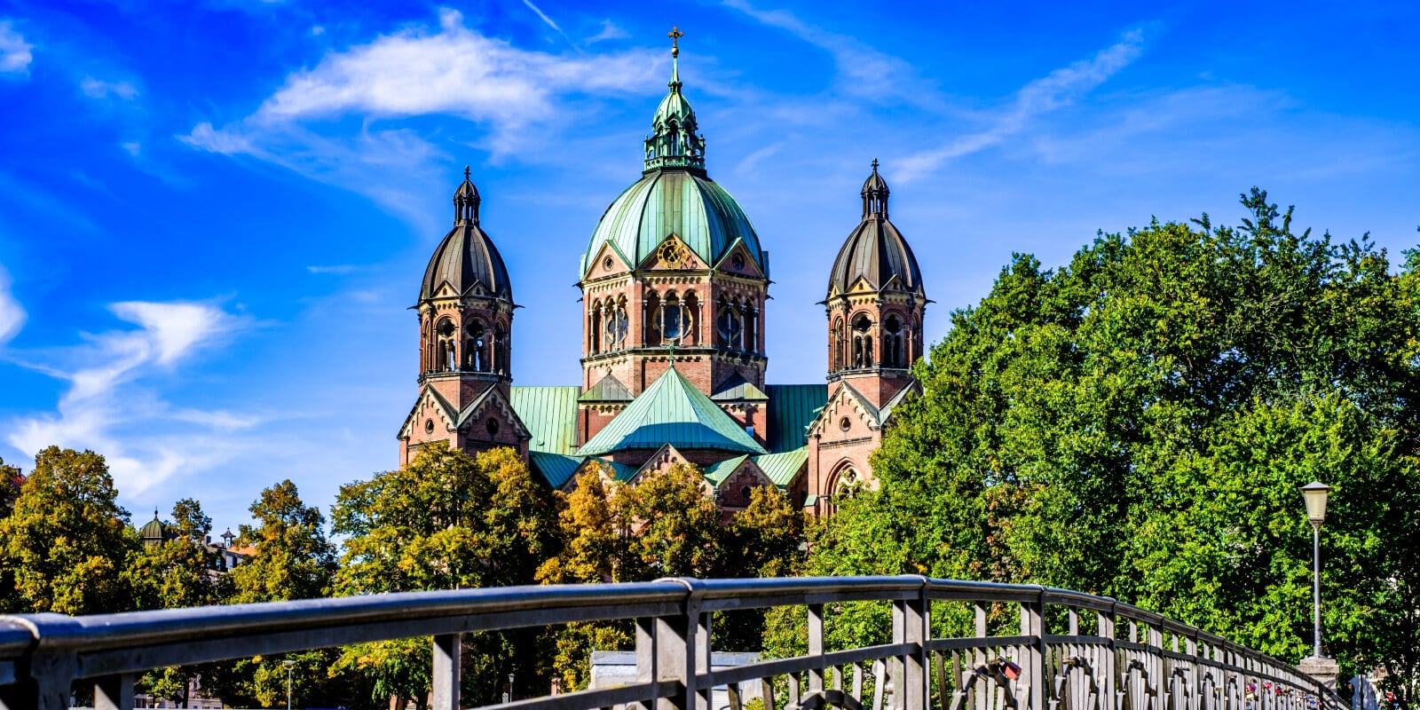 Lukaskirche in München mit Brücke über die Isar unter blauem Himmel.