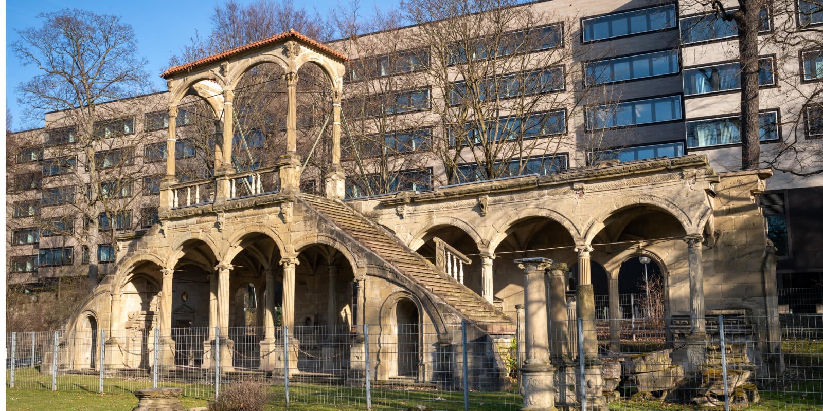 Historisches Römisches Theater in Stuttgart mit Arkaden und Freitreppe vor modernen Gebäuden.